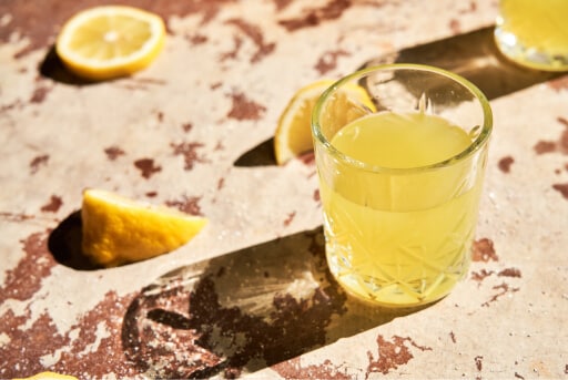 Limoncello glaasje op een stenen ondergrond met citroenpartjes eromheen